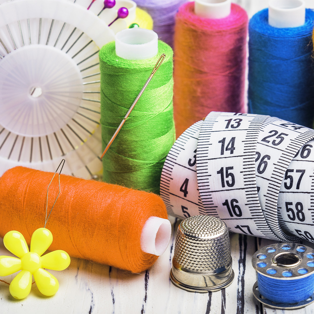 Nähmaterial & Kurzwaren Buntes Nähzubehör-Set mit Garnrollen, Maßband, Fingerhut und Nadeln auf einer Holzoberfläche