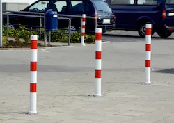 Herausnehmbare Absperrpfosten, die einen Fußgängerdurchgang an einem Parkplatz abgrenzen.