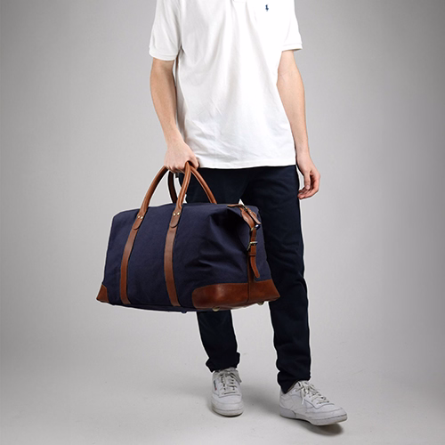 SID and VAIN Reisetasche LENNOX Canvas und Leder in blau braun Indoor Mann traegt schwarze Hose und weißes T-Shirt