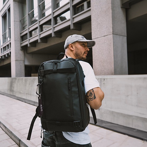 Sons of ALOHA Rucksack AHI in schwarz Outdoor Mann traegt graue Jeans mit weißem T-Shirt und Cap