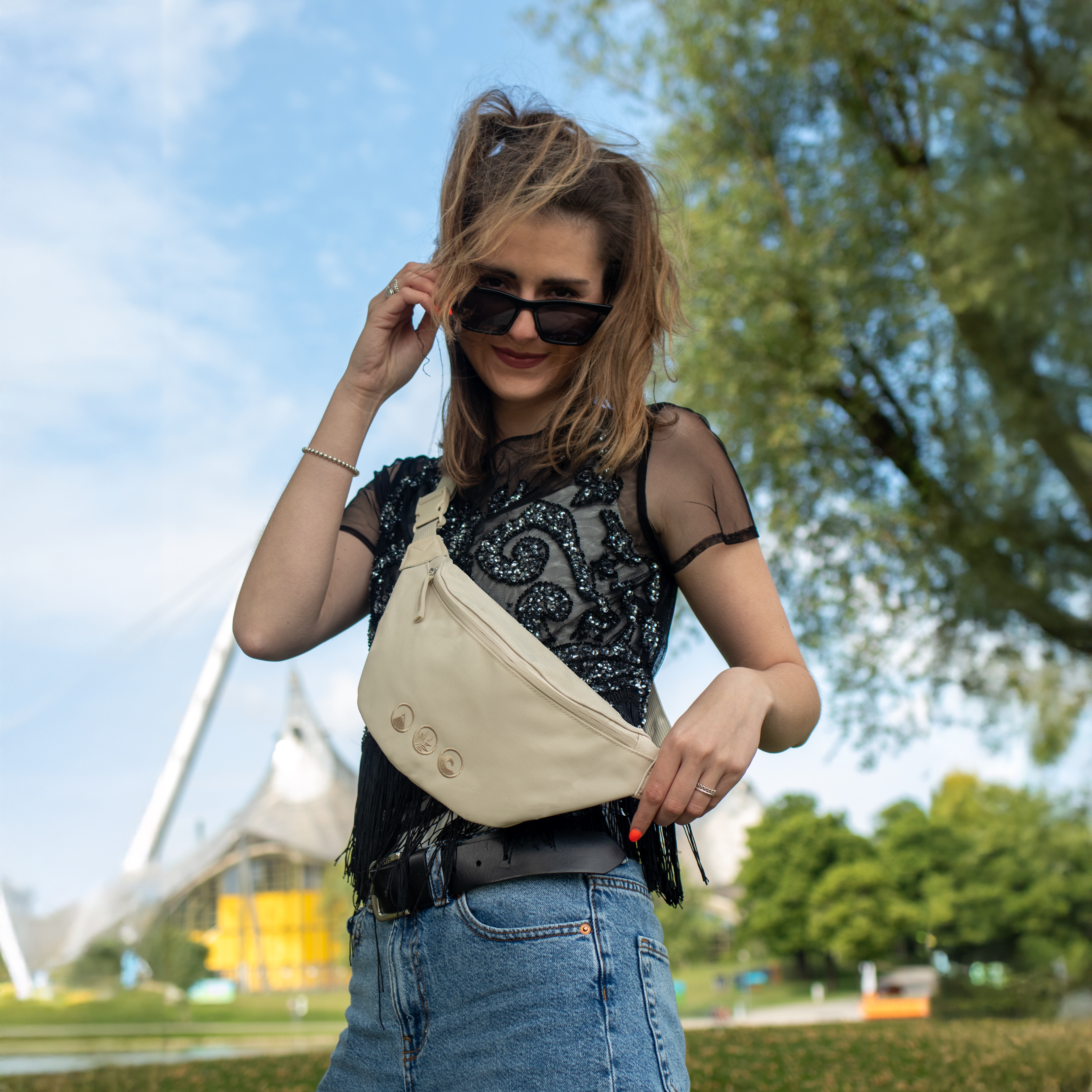 Sons of Aloha Bauchtasche LEI in beige aus recyceltem Material Outdoor Frau traegt kurzes schwarzes Fransenoberteil zu einer weiten Jeans