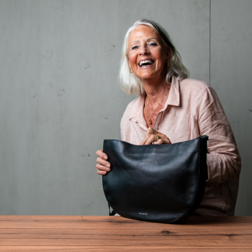 FEYNSINN Handtasche Leder schwarz Indoor Frau sitzt am Tisch und lacht 