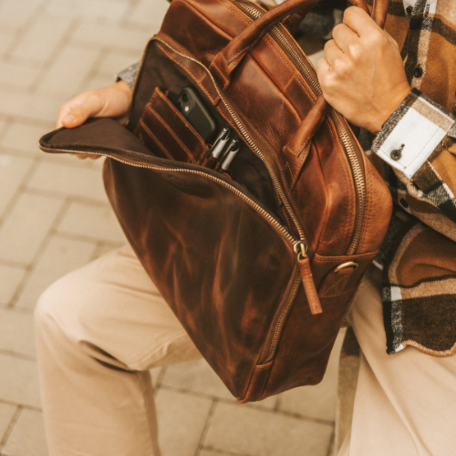 SID and VAIN Laptoptasche Leder SIMON in braun Outdoor Mann sitzt und oeffnet die Laptoptasche