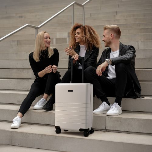 Feynsinn Handgepäck Koffer beige Ryker Outdoor zwei Frauen und ein Mann sitzen draußen auf einer Treppe