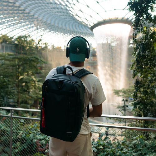 SONS OF ALOHA Mann traegt einen rucksack AHI in schwarz auf dem Rücken und hat Kopfhörer auf
