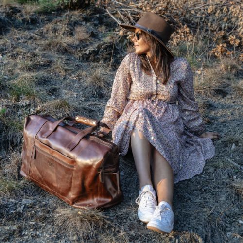 Sid & Vain Reisetasche Leder Bristol cognac braun Outdoor Frau sitzt in der Wiese und traegt ein sommerliches Kleid