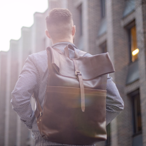 Sid and Vain Uni Rucksack Herren JAY Leder in dunkelbraun Outdoor Mann steht vor einem Gebaeude und traegt eine karierte Jacke