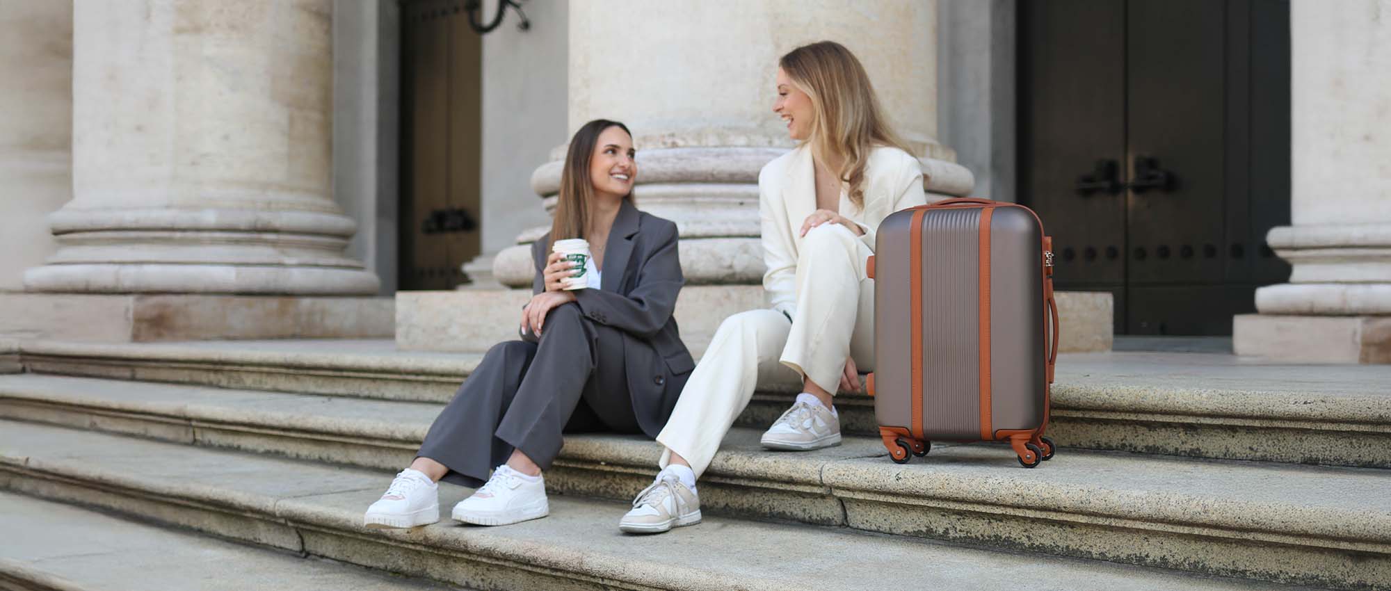 Suitcase from a luggage set next to two women sitting on stairs in Rome