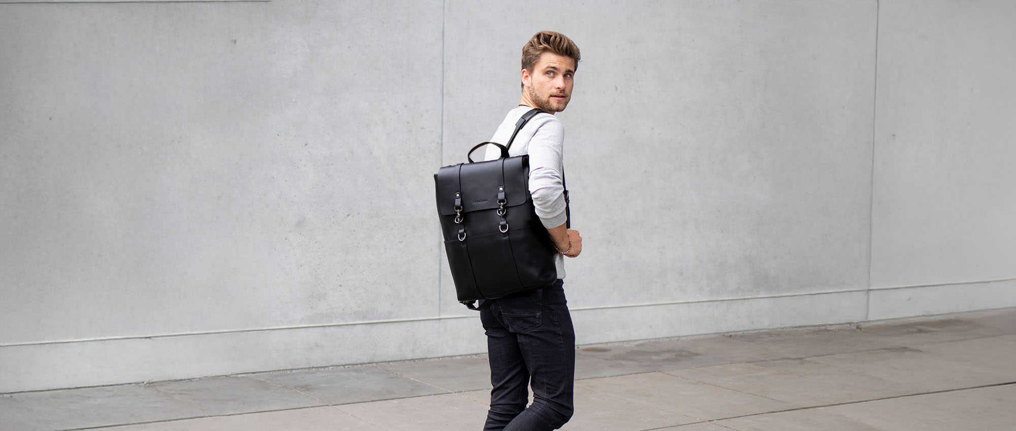 Black laptop backpack worn by a man in a smart casual sweater and jeans