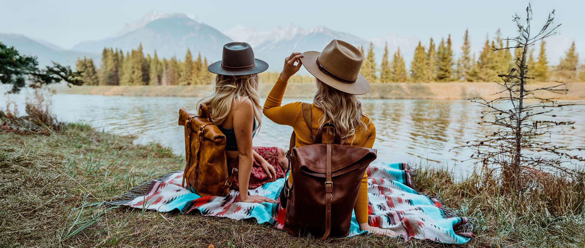 Brown leather backpack and two women sitting by a lake