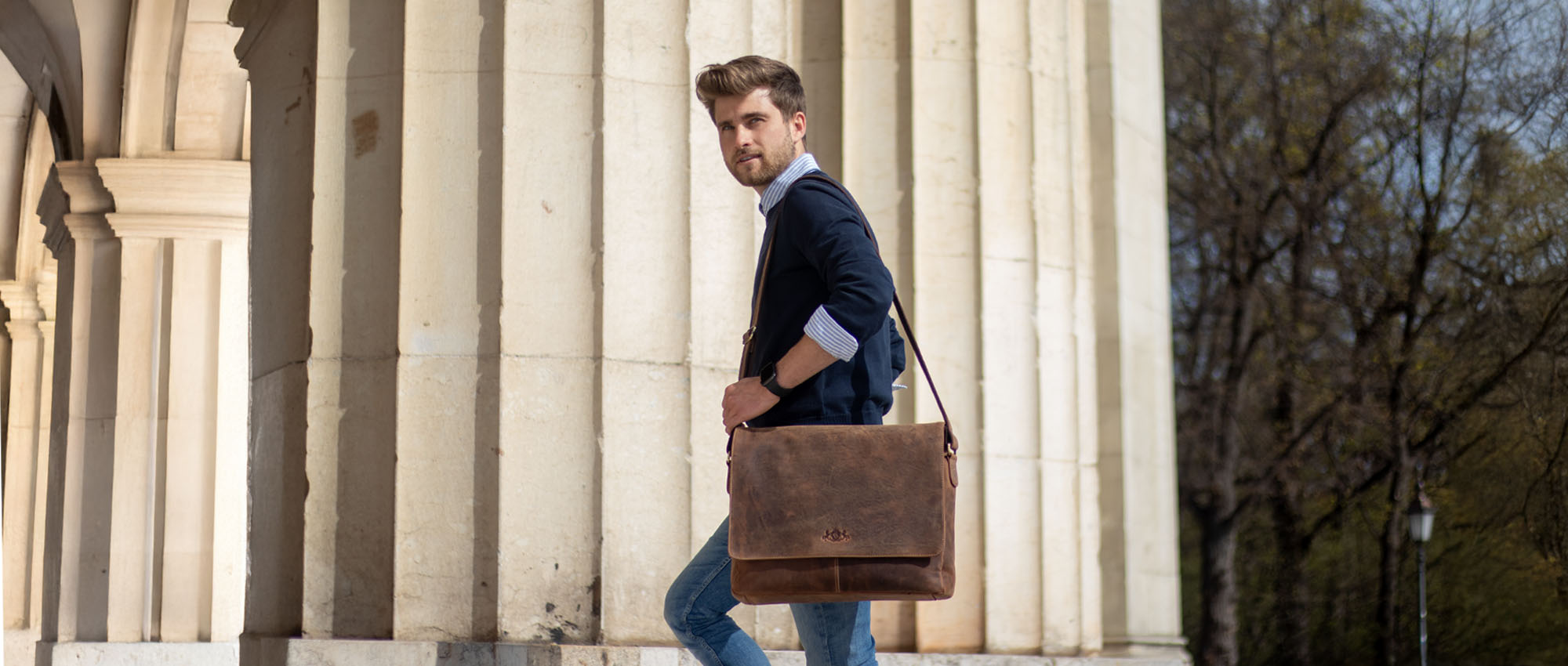 Leather messenger bag on a man in a shirt, sweater, and jeans