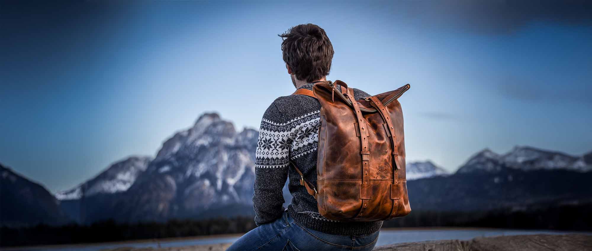 Sac à dos en cuir pour homme, homme portant un pull assis sur des rochers