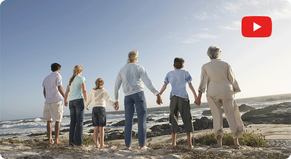 Eine Großfamilie hält sich am Strand an den Händen und blickt auf das Meer. Das Bild symbolisiert familiären Zusammenhalt und hohe Lebensqualität durch Homecare. Rechts oben im Bild ist ein roter YouTube Button dargestellt.