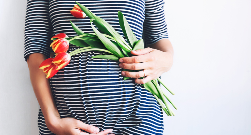 Schwangere Frau mit gelb-roten Tulpen in der Hand