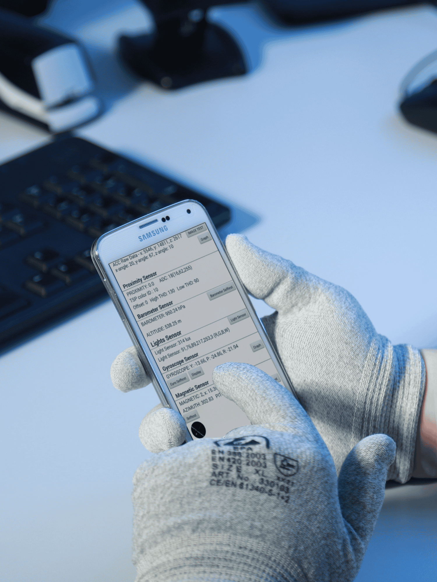 A person wearing light-colored work gloves is holding a smartphone in both hands, operating it. The phone displays a checklist or list of items.