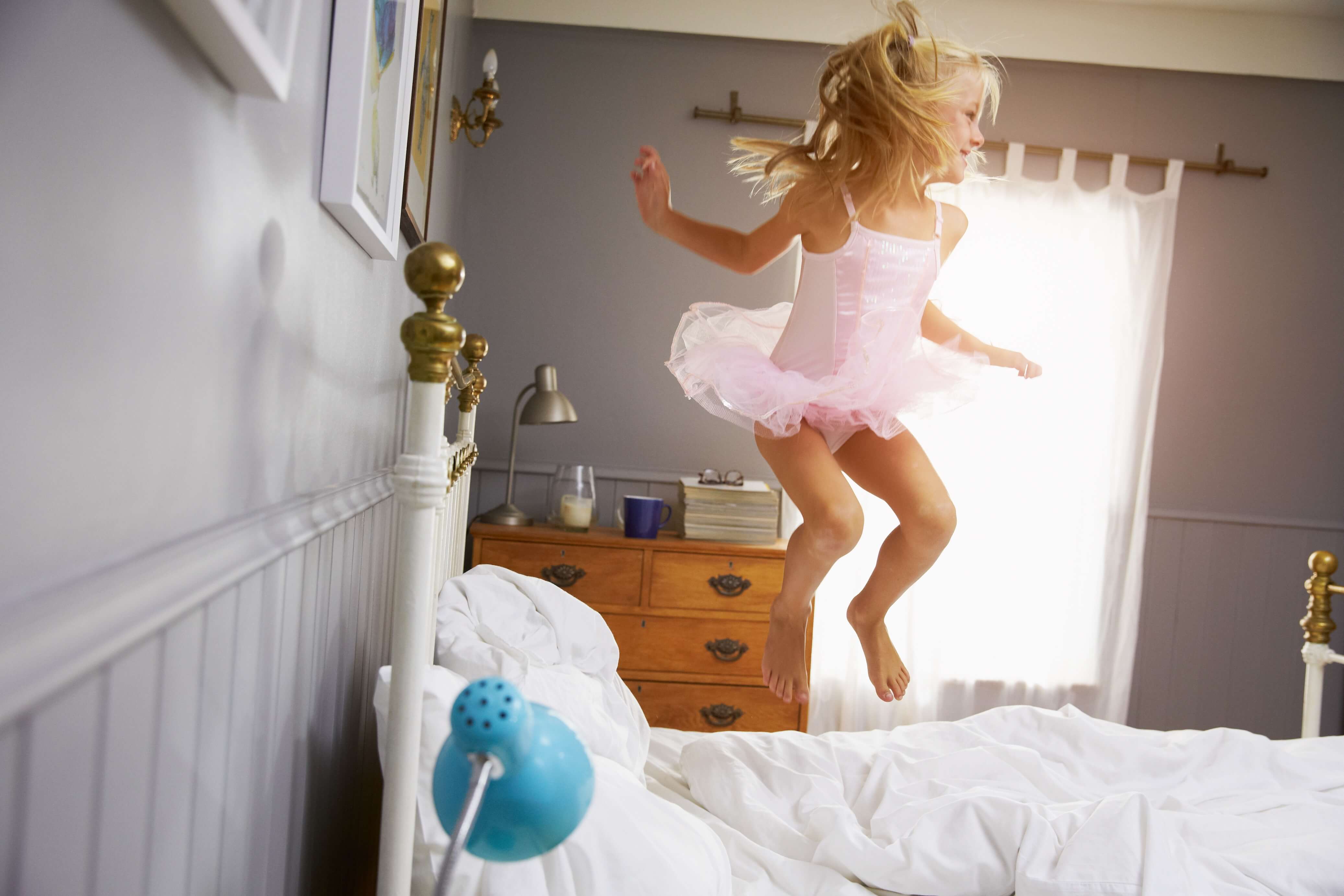 Kind springt lachend auf dem Bett – energiegeladen und voller Vorfreude