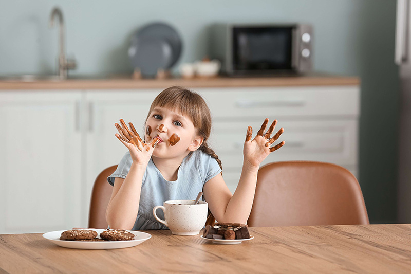  Girl eating cake, chocolate on her hands, and with a smiling face