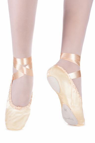 Nahaufnahme der Füße einer Ballerina in rosa Ballettschuhen aus Satin und Strumpfhosen