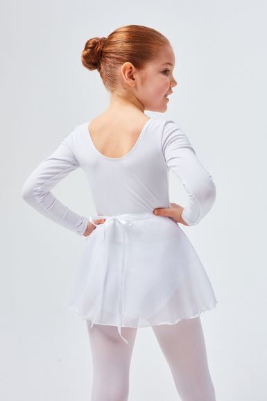 Ein junges Mädchen in einem weißen Ballett-Outfit steht mit den Händen in den Hüften und blickt leicht zur Seite.