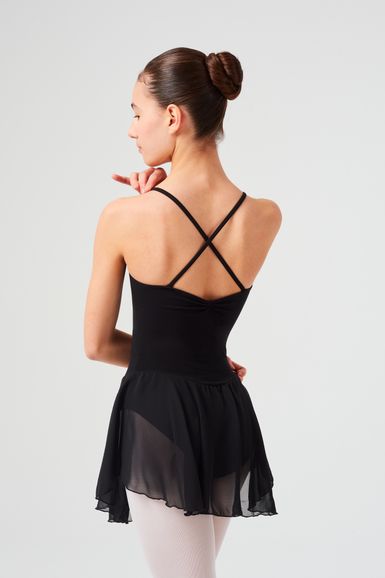 Eine Frau in einem schwarzen Ballettanzug und Rock steht mit dem Rücken zur Kamera und zeigt nach rechts.