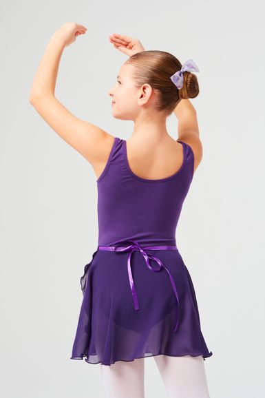 Ein Mädchen in einem lila Ballett-Outfit posiert mit erhobenen Armen und blickt von der Kamera weg.