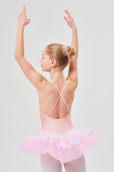 Ein Mädchen in einem rosa Ballett-Tutu steht mit erhobenen Armen und blickt von der Kamera weg.