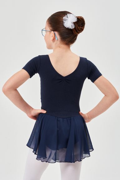 Mädchen in marineblauem Ballett-Outfit und weißen Strumpfhosen steht mit den Händen in den Hüften und blickt von der Kamera weg.