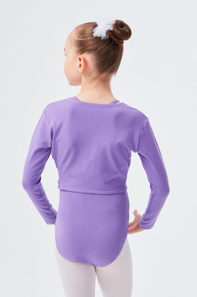 Ein junges Mädchen in einem lavendelfarbenen Langarmbody und weißen Strumpfhosen steht mit den Händen in den Hüften und blickt von der Kamera weg.