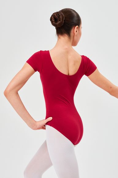 Eine Balletttänzerin in einem roten Ballett Trikot und weißen Strumpfhosen posiert mit ausgestrecktem Arm