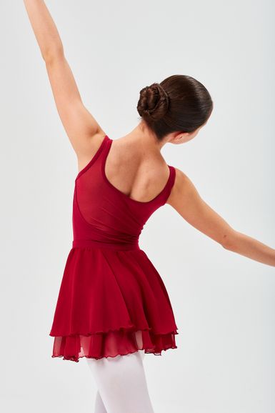 Person in rotem Ballettkleid und weißer Strumpfhose posiert mit ausgestreckten Armen und blickt von der Kamera weg.