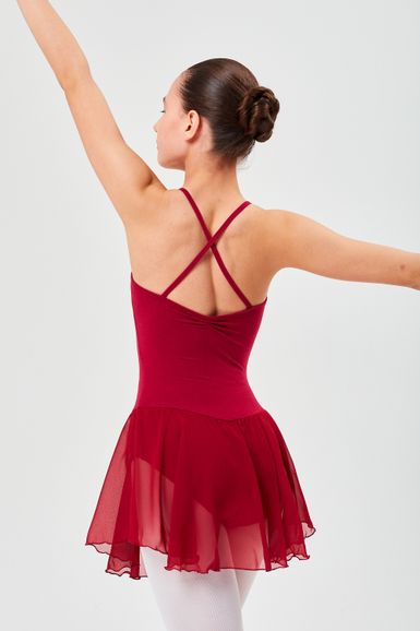 Eine Tänzerin in einem roten Ballett Trikot und Rock steht mit erhobenen Armen und blickt von der Kamera weg.