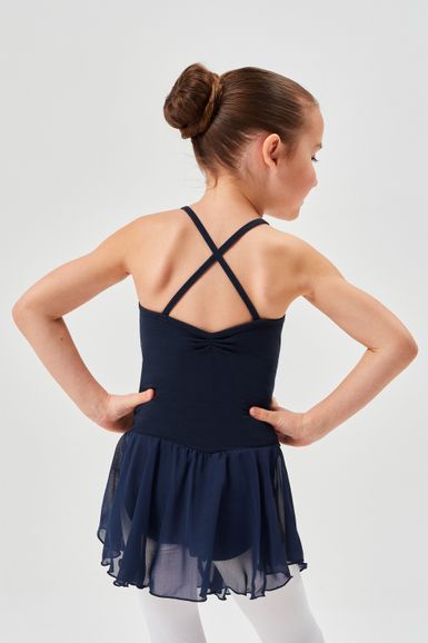 Ein junges Mädchen in einem marineblauen Ballettkleid mit überkreuzten Trägern steht mit den Händen in den Hüften und blickt von der Kamera weg.
