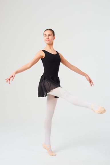 Eine Balletttänzerin in einem schwarzen Ballett Trikot und weißen Strumpfhosen führt eine Pose mit einem angehobenen Bein und ausgestreckten Armen aus.