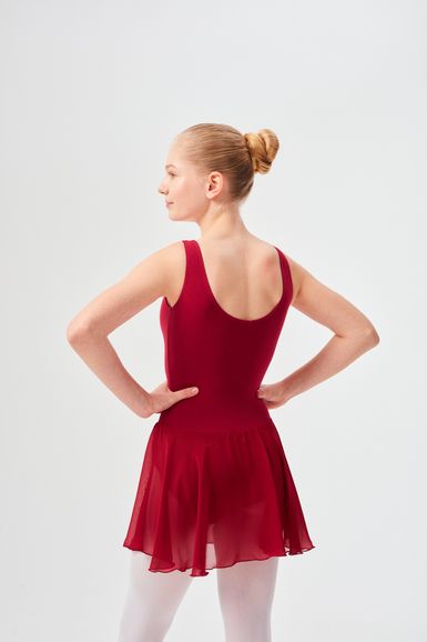 Eine Person in einem roten Ballett Trikot und Rock steht mit den Händen in den Hüften und blickt von der Kamera weg.