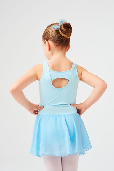 Ein junges Mädchen in einem hellblauen Ballett Trikot und Rock steht mit den Händen in den Hüften und blickt von der Kamera weg.
