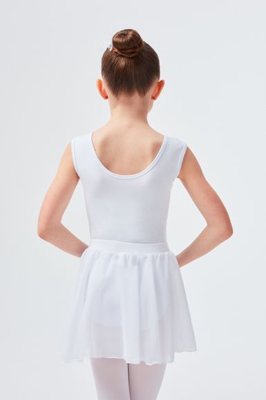 Ein junges Mädchen in einem weißen Ballett-Outfit steht mit abgewandtem Blick und den Händen in den Hüften.