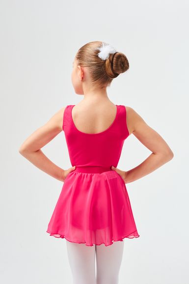 Ein junges Mädchen in einem leuchtend rosa Ballett-Outfit steht mit den Händen in den Hüften und blickt von der Kamera weg.