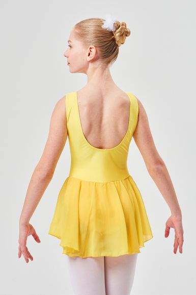Ein Mädchen in einem gelben Ballettkleid mit Duttfrisur steht mit abgewandtem Gesicht da
