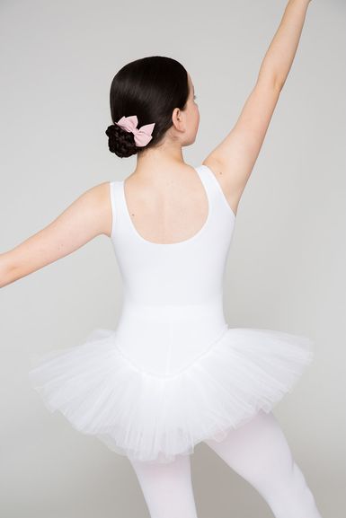 Eine Balletttänzerin in einem weißen Ballett Trikot und Tutu posiert mit erhobenen Armen und blickt von der Kamera weg.