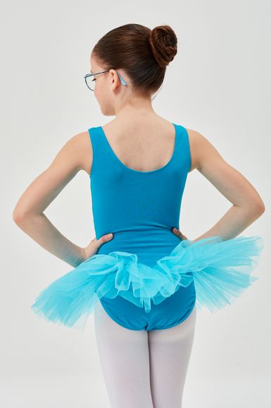 Ein Mädchen in einem blauen Ballett Trikot und Tutu steht mit den Händen in den Hüften und blickt von der Kamera weg.