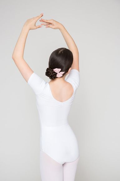 Eine Balletttänzerin in einem weißen Ballett Trikot steht mit erhobenen Armen da