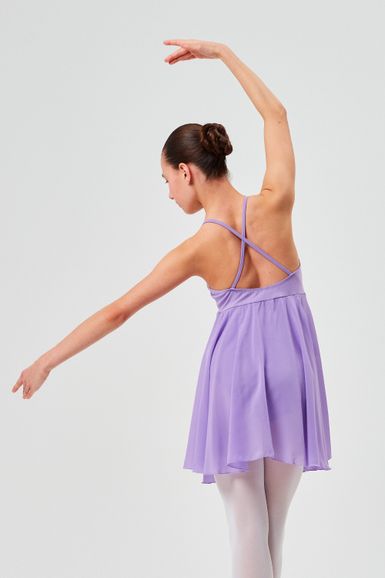 Eine Balletttänzerin in einem lavendelfarbenen Kleid und weißen Strumpfhosen posiert mit erhobenen Armen und einem angewinkelten Arm