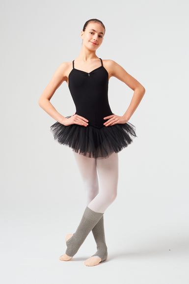 Eine Ballerina in einem schwarzen Ballett Trikot und Tutu posiert mit den Armen in den Hüften und trägt weiße Strumpfhosen und graue Beinwärmer.