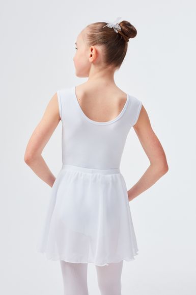 Ein junges Mädchen in einem weißen Ballett-Outfit steht mit den Händen in den Hüften und blickt von der Kamera weg.