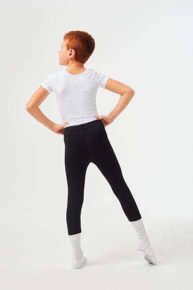 Ein Junge in einem weißen Hemd und schwarzen Leggings steht in einer Ballettpose.