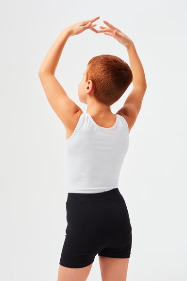 Ein Kind in einem weißen Tanktop und schwarzen Shorts hebt die Arme über den Kopf und blickt von der Kamera weg.