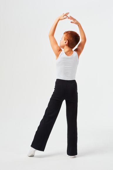 Ein Kind in einem weißen Tanktop und einer schwarzen Hose steht mit erhobenen Armen auf einem Bein und posiert.