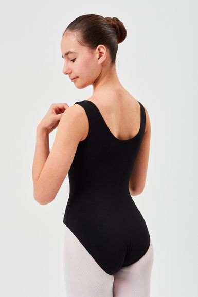 Eine Person in einem schwarzen Ballett Trikot und hellen Strumpfhosen steht in einer Ballettpose und blickt von der Kamera weg.