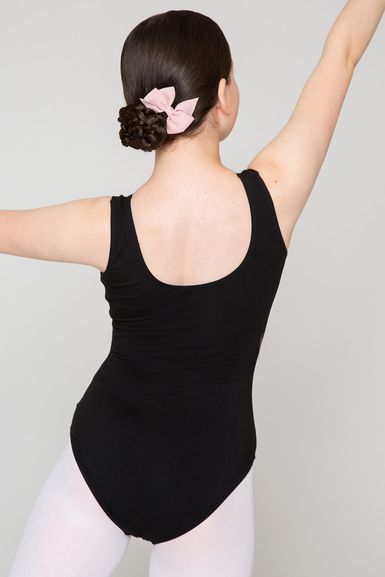 Eine Balletttänzerin in einem schwarzen Trikot und einer rosa Schleife posiert mit ausgestreckten Armen und blickt von der Kamera weg.