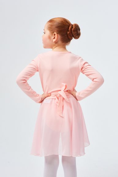 Ein junges Mädchen in einem rosa Ballett-Outfit steht mit den Händen in den Hüften und blickt von der Kamera weg.